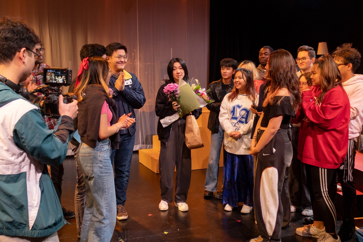 An actor receives flowers and attention from the audience and ensemble. 